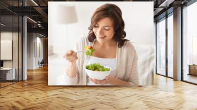 smiling young woman eating salad at home Wall mural