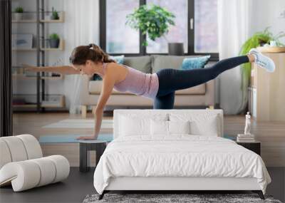 sport, fitness and exercising concept - happy young woman doing elbow knee crunches at home Wall mural