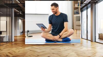 sport, fitness and healthy lifestyle concept - man with tablet computer sitting on exercise mat at home Wall mural