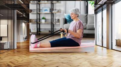 sport, fitness and healthy lifestyle concept - smiling senior woman exercising with resistance band on mat at home Wall mural