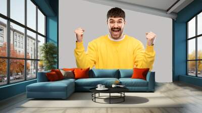 success, emotion and expression concept - happy man in yellow sweatshirt celebrating victory over grey background Wall mural