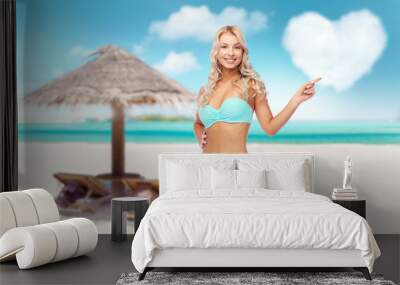 summer holidays, vacation and travel concept - happy smiling young woman in bikini swimsuit pointing finger over tropical beach of maldives background Wall mural