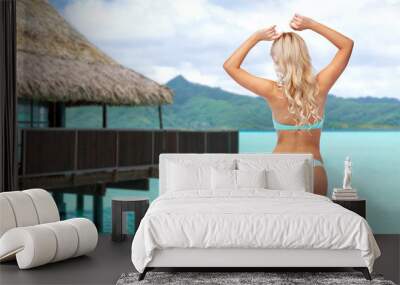 summer holidays, vacation and travel concept - young woman posing in bikini over bungalow on tropical beach background in french polynesia Wall mural