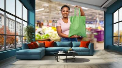 sustainability and people concept - happy smiling young african american woman with green reusable canvas bag for food shopping over grocery store or supermarket background Wall mural