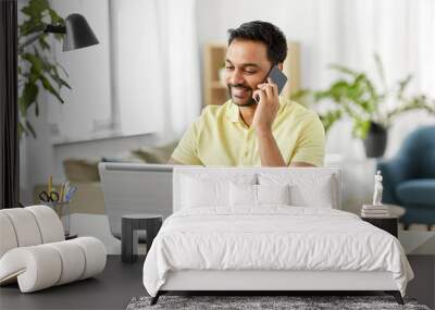 technology, communication and remote job concept - happy smiling indian man calling on smartphone with laptop computer working at home office Wall mural