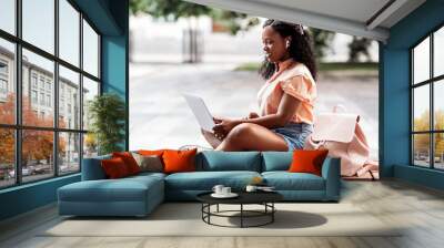 technology, education and people concept - happy smiling african american student girl in earphones with laptop computer and books in city Wall mural