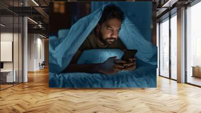 technology, internet, communication and people concept - young indian man with smartphone lying in bed under blanket at home at night Wall mural