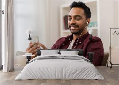 technology, leisure and people concept - happy man in earphones with smartphone listening to music at home Wall mural