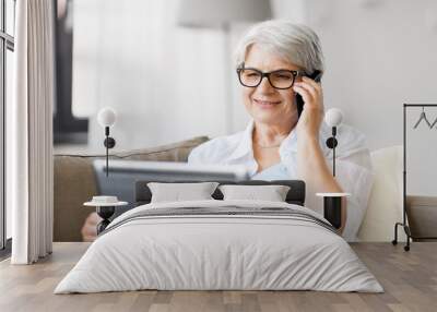 technology, old age and people concept - happy senior woman in glasses with laptop computer calling on smartphone at home Wall mural