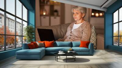 technology, old age and people concept - happy senior woman with laptop computer at home in evening Wall mural