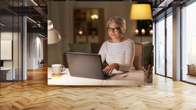 technology, old age and people concept - senior woman in glasses with laptop working at home in evening Wall mural