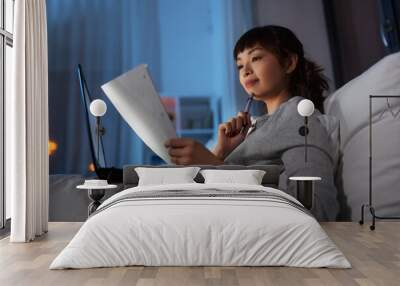 technology, remote job and people concept - young asian woman with laptop computer and papers working in bed at home at night Wall mural