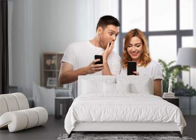 technology and people concept - happy couple in white t-shirts with smartphones over home background Wall mural