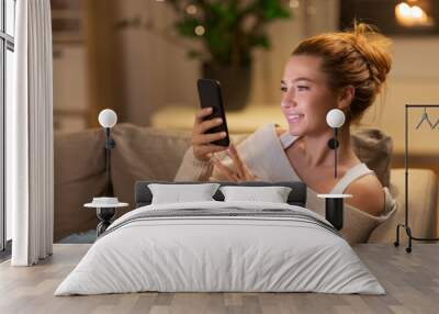 technology and people concept - happy young woman with smartphone at home in evening Wall mural