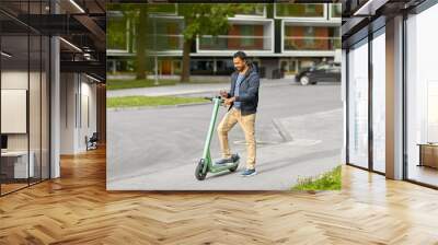 transport, technology and people and concept - happy smiling young man with electric scooter using smartphone on city street Wall mural