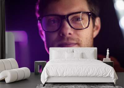 vision, eyewear and people concept - portrait of smiling young man in glasses over ultra violet neon lights in dark room Wall mural