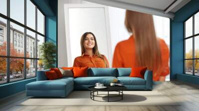 wardrobe, fashion, style and people concept - happy woman in orange shirt looking at mirror reflection at home or clothing store dressing room Wall mural