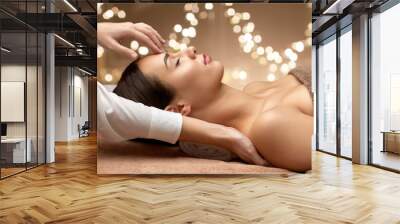 wellness, beauty and relaxation concept - beautiful young woman lying with closed eyes and having face and head massage at spa over festive lights on background Wall mural