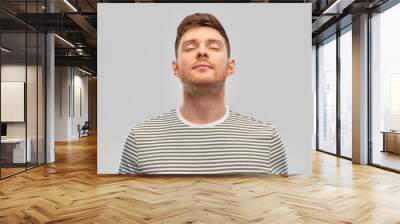 wellness and people concept - happy young man in striped t-shirt breathing over grey background Wall mural