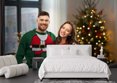 winter holidays, celebration and people concept - portrait of happy couple in ugly sweaters at home over christmas tree lights background Wall mural