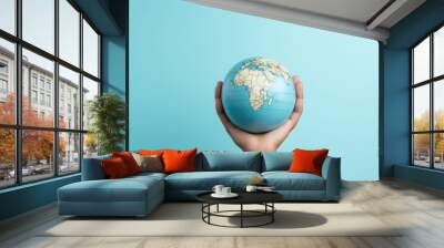 Hand gently holding a globe against a vibrant blue background, symbolizing the spirit of global travel and exploration on world tourism day. Copy space Wall mural