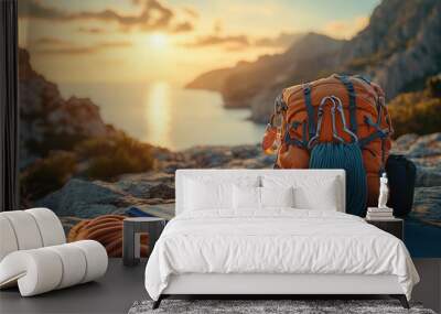 Sunset over tranquil ocean bay with orange backpack and climbing gear on a rock, evoking feelings of adventure, peace, and natural beauty Wall mural