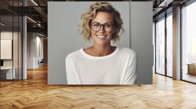 Young adult stylish confident attractive smiling blonde European business woman, beautiful lady pretty model with curly blond hair wearing glasses looking at camera, close up face portrait indoors. Wall mural