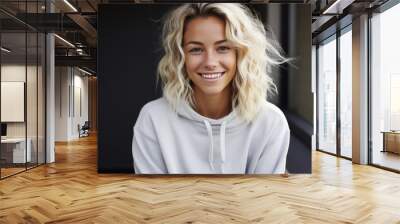 Young adult stylish smiling blonde European woman, beautiful teen girl pretty gen z model with curly blond hair wearing hoodie looking at camera, close up face street style portrait outdoors. Wall mural