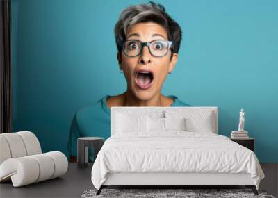 Young beautiful woman wearing elegant blue sweater and glasses and blue jacket over isolated background afraid and shocked with surprise expression, fear and excited face face with. Wall mural