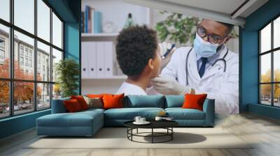 Male pediatrician using flashlight to examine little boy's throat, visit to the doctor Wall mural