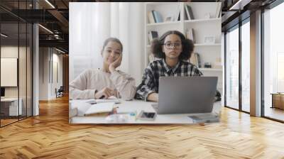 Portrait of clever teen students doing homework together, sitting at desk with laptop and books, education Wall mural