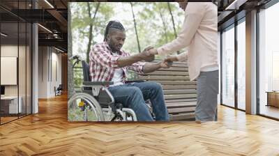 Young woman helping man to get up from wheelchair, recovery after injury Wall mural