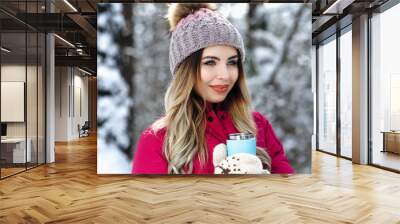 pretty woman drink hot  beverage from blue hermocouple. She hold cup in her hands which wear knitted gloves. Winter holiday concept. Wall mural