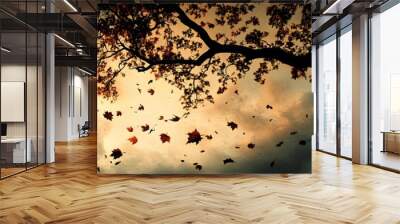 The silhouette of a maple tree with leaves falling around it, set against a dusky sky. The scene captures the essence of autumn's transition. Wall mural