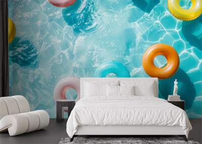 Top view of inflatable swimming rings on a sunlit turquoise pool, depicting summer leisure and fun. colorful pool scene with floaties Wall mural