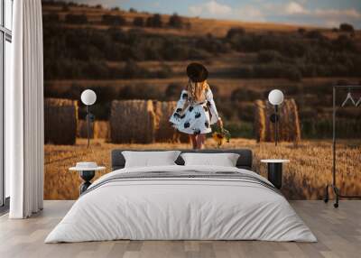 Happy young woman in white dress walking in sunset field with hay bales, beautiful romantic girl with long hair outdoors in field. Wall mural