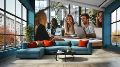 Smiling Team Collaborating in a Modern Office. A diverse team of young professionals works together on laptops in a bright and modern office space. Wall mural