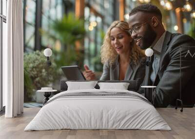 Two professionals engaged in a discussion over a tablet in a modern office cafe. Wall mural