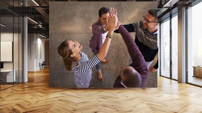 Heres to success. High angle shot of a group of work colleagues engaging in high fives in a circle in the office. Wall mural