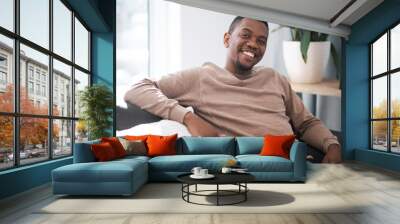 Relax, smile and portrait of black man on sofa at home in city apartment. Happy, healthy and proud man and leader in business from South Africa smiling and relaxing alone on couch in living room. Wall mural