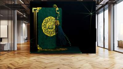 Green cover Holy Quran with arabic word Allah meaning The One and Only God and tasbih or rosary beads over black background. Wall mural