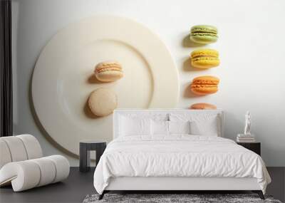 Two light macaroons on a light plate and a row of macarons of different colors on a white table, top view Wall mural