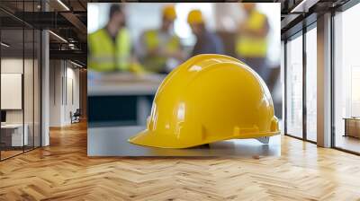 Close-up of a yellow hard hat on a table at a construction site meeting with workers. Wall mural