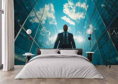 Confident man in a suit walking between modern glass buildings under a clear blue sky. Wall mural