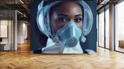 Portrait African American beautiful woman doctor in medical mask, face shield and goggles looking at camera. Close up female physician in respiratory protection. Doctors on background. Protected suit Wall mural