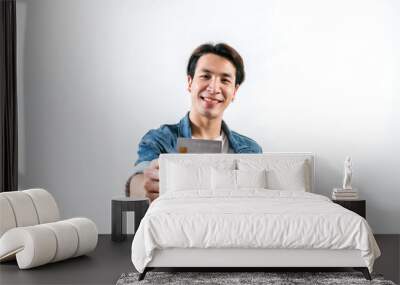 A young man smiles and looks happy with a credit card in hand, he is looking away while showing and thinking of a new card. An internet wireless Online technology and online shopping concept idea Wall mural