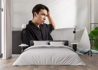 Anxiety Young man student or businessman talking a solution for financial crisis work problems working on a computer laptop at a home office for video conference, sits on a couch, looking on a screen Wall mural