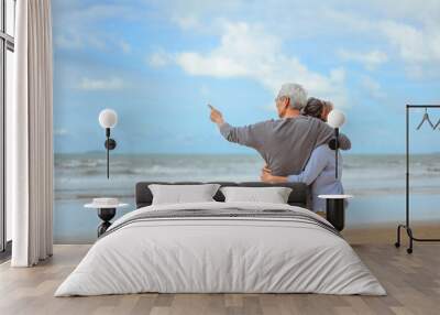 A senior couple hugged each other at the beach in the morning. The old man pointed the finger to the old woman to look at the bright blue sky, life insurance plan at the retirement concept. Wall mural