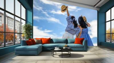 Two happy woman holding straw hat with hand raised to sky. Wall mural