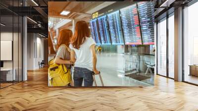 Two women in international airport terminal, looking at information board, checking her flight. Wall mural